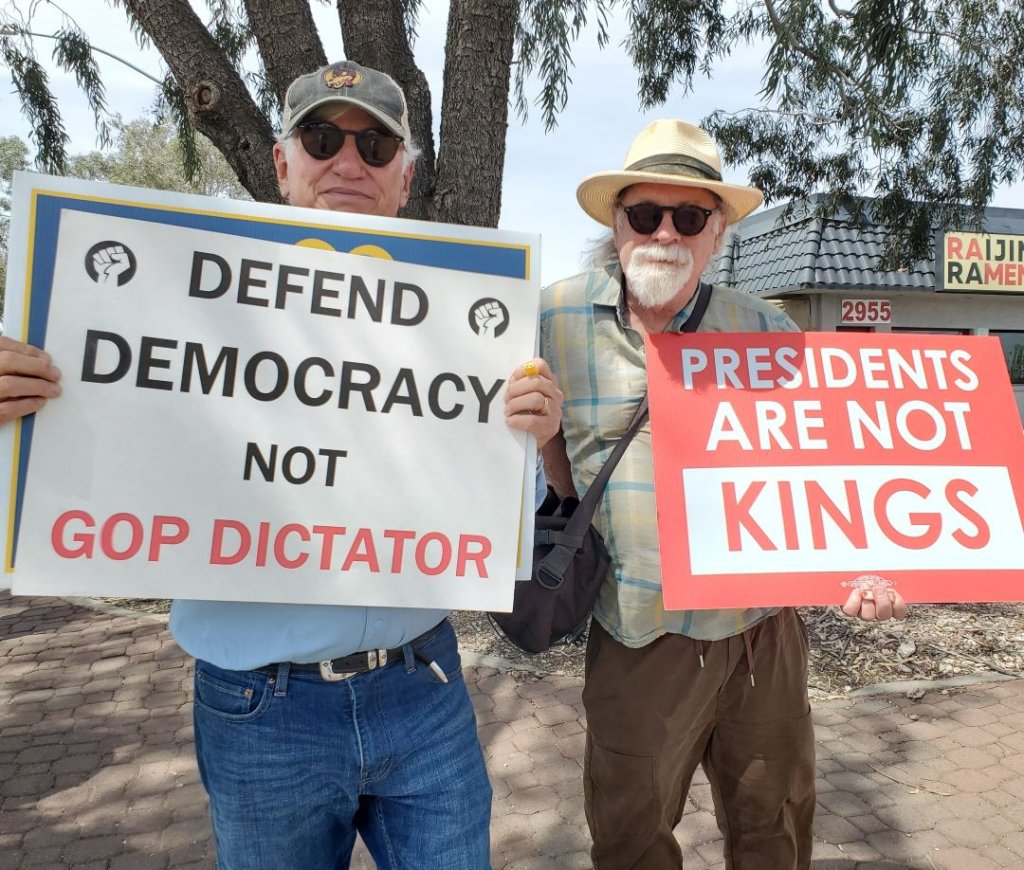 TWo men holding signs at No Kings protest along Speedway