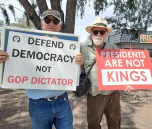 TWo men holding signs at No Kings protest along Speedway
